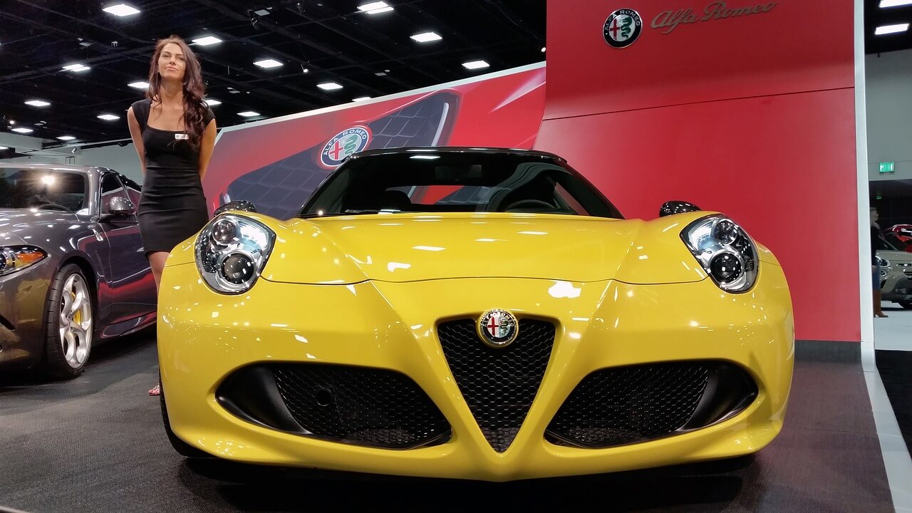 A yellow Alfa Romeo and a woman next to it at a car show