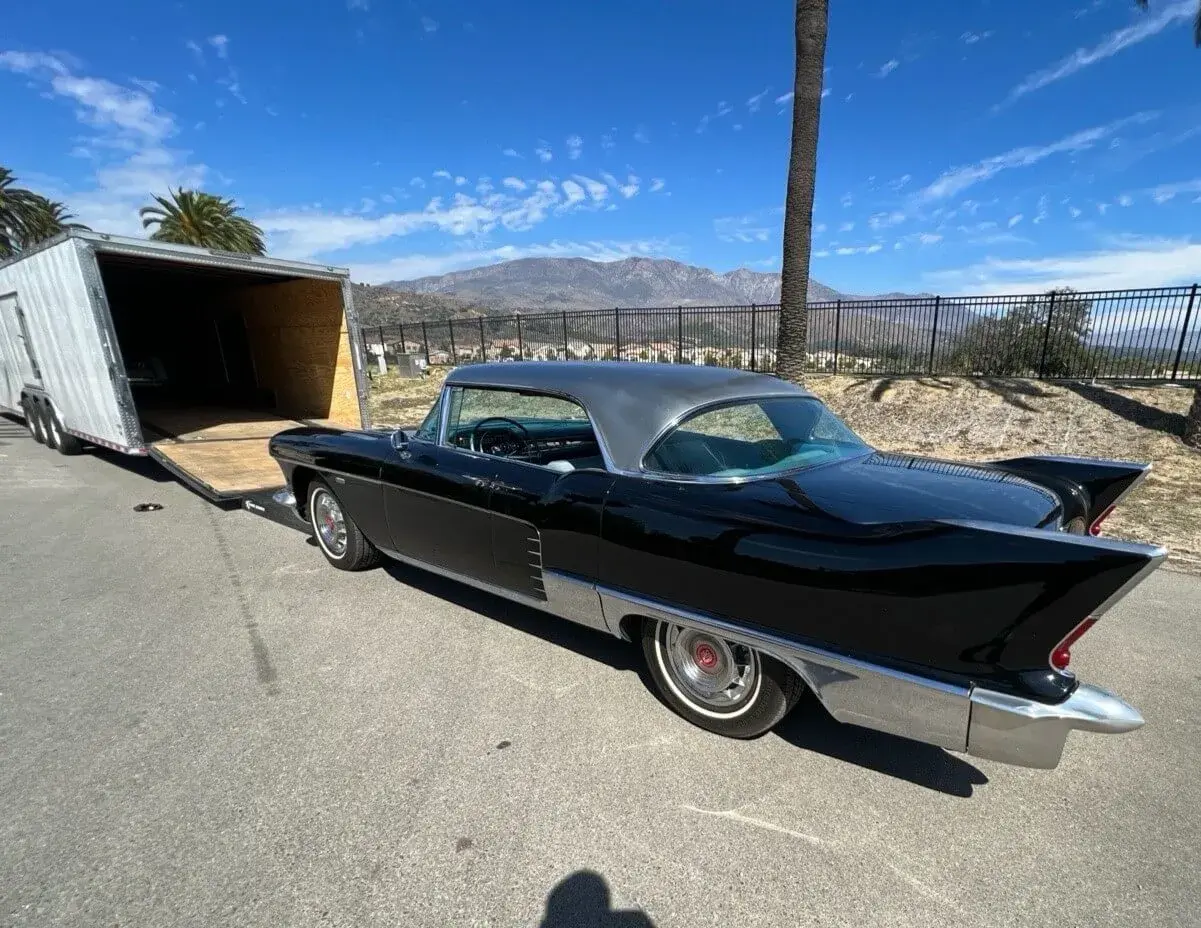 A black vintage car getting into an enclosed trailer