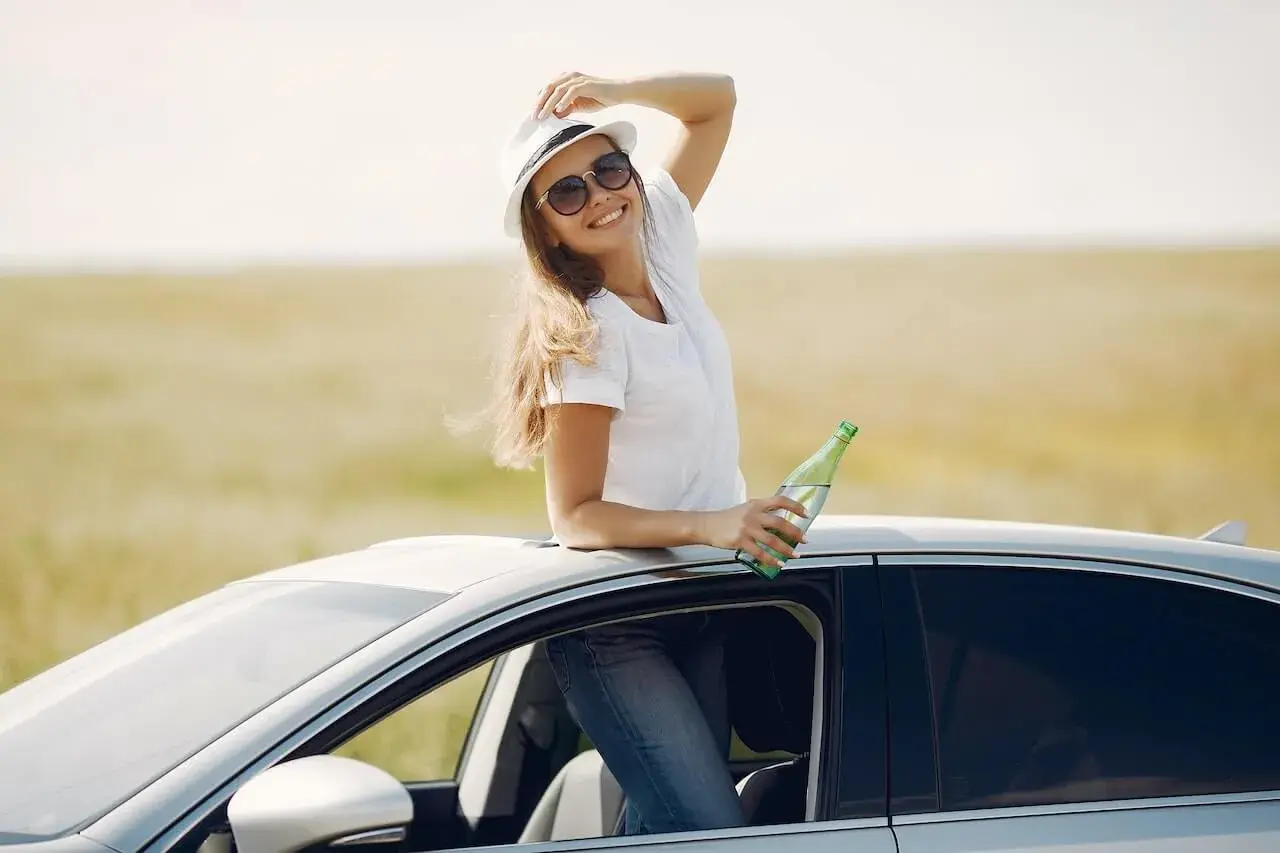 Cheerful young woman with refreshing drink in automobile during car trip
