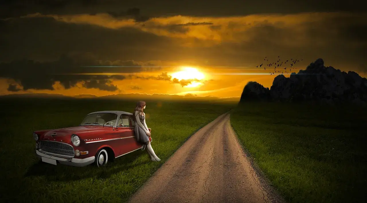 Red car with a girl next to it and the sunset behind